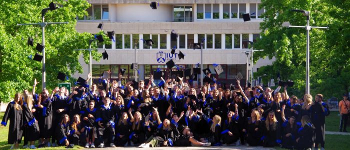 Photo d'une remise des diplômes : les étudiants sont en tenue de diplômés sur le parvis de l'IUT d'Annecy