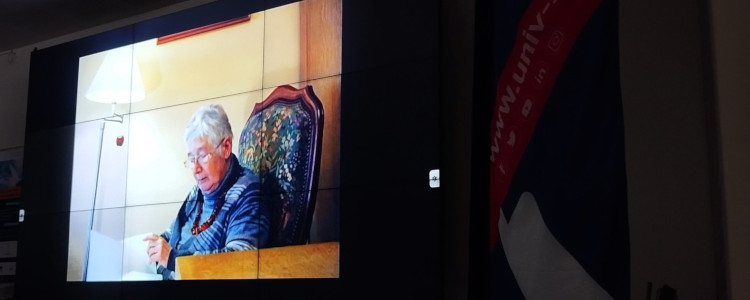 Une dame âgée dans un fauteuil est représentée sur un écran au centre d'une salle, pour la projection d'un documentaire.